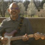 Steve setting on deck with guitar.